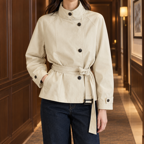 Woman wearing an off white belted jacket with a high stand collar and offset buttons