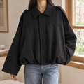 Woman wearing a black cropped bomber jacket with a pointed collar and gathered hem