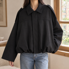 Woman wearing a black cropped bomber jacket with a pointed collar and gathered hem