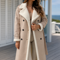 A woman wears a beige double breasted coat with plush contrast lapels, front buttons and a longline cut.