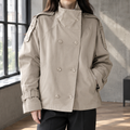Woman wearing a khaki double breasted jacket with a stand collar and shoulder epaulettes