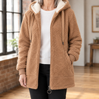 A woman wears a brown hooded jacket with plush texture, a cream lined hood and front zipper.