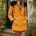 A woman wears a gold hooded parka coat with plush hood trim, front buttons and waist tabs.