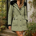 A woman wears a green hooded parka coat with plush hood trim, front buttons and waist tabs.