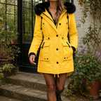 A woman wears a yellow hooded parka coat with plush hood trim, front buttons and waist tabs.