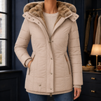 A woman wears a beige hooded puffer jacket with a plush lined hood, quilted body and zip pockets.