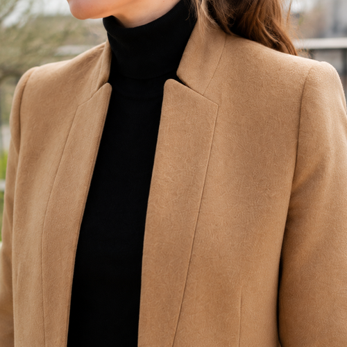 Close view of a beige mandarin collar coat showing raised collar, tailored shoulders and clean front edge.