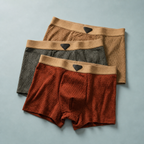 Three boxer briefs arranged in tan, gray and rust red with wide elastic waistbands.