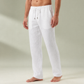 White mens linen pants with a drawstring waistband and relaxed full length legs, shown barefoot.