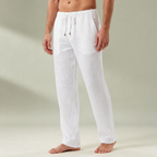 White mens linen pants with a drawstring waistband and relaxed full length legs, shown barefoot.