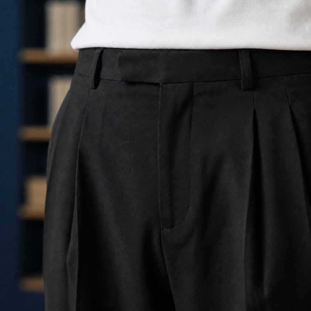 Black pleated pants showing the front waist and pleats beneath a white shirt.