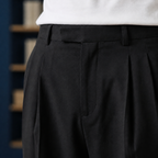 Black pleated pants showing the front waist and pleats beneath a white shirt.