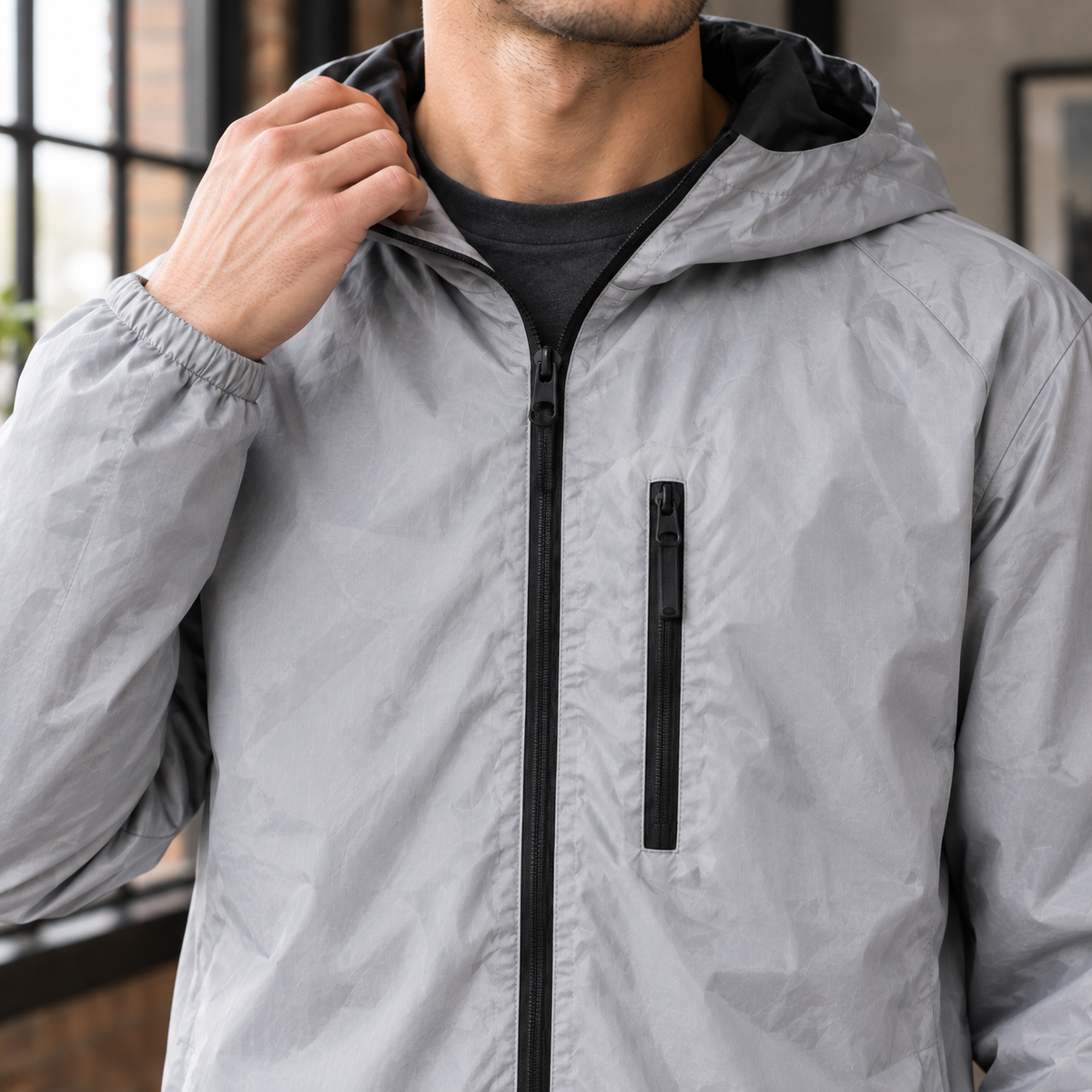 Reflective Hooded Jacket detail view 2 showing the reflective silver-gray finish, hood, and zipped chest pocket.