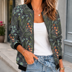 A woman wears a dark gray printed bomber jacket with a botanical pattern, front zip and ribbed trim.