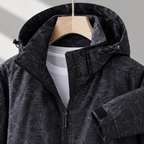 Close view of the black printed jacket showing its drawcord hood and zipped side pockets