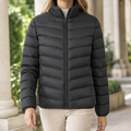 A woman wears a black quilted puffer jacket with chevron quilting, a stand collar and front zip.