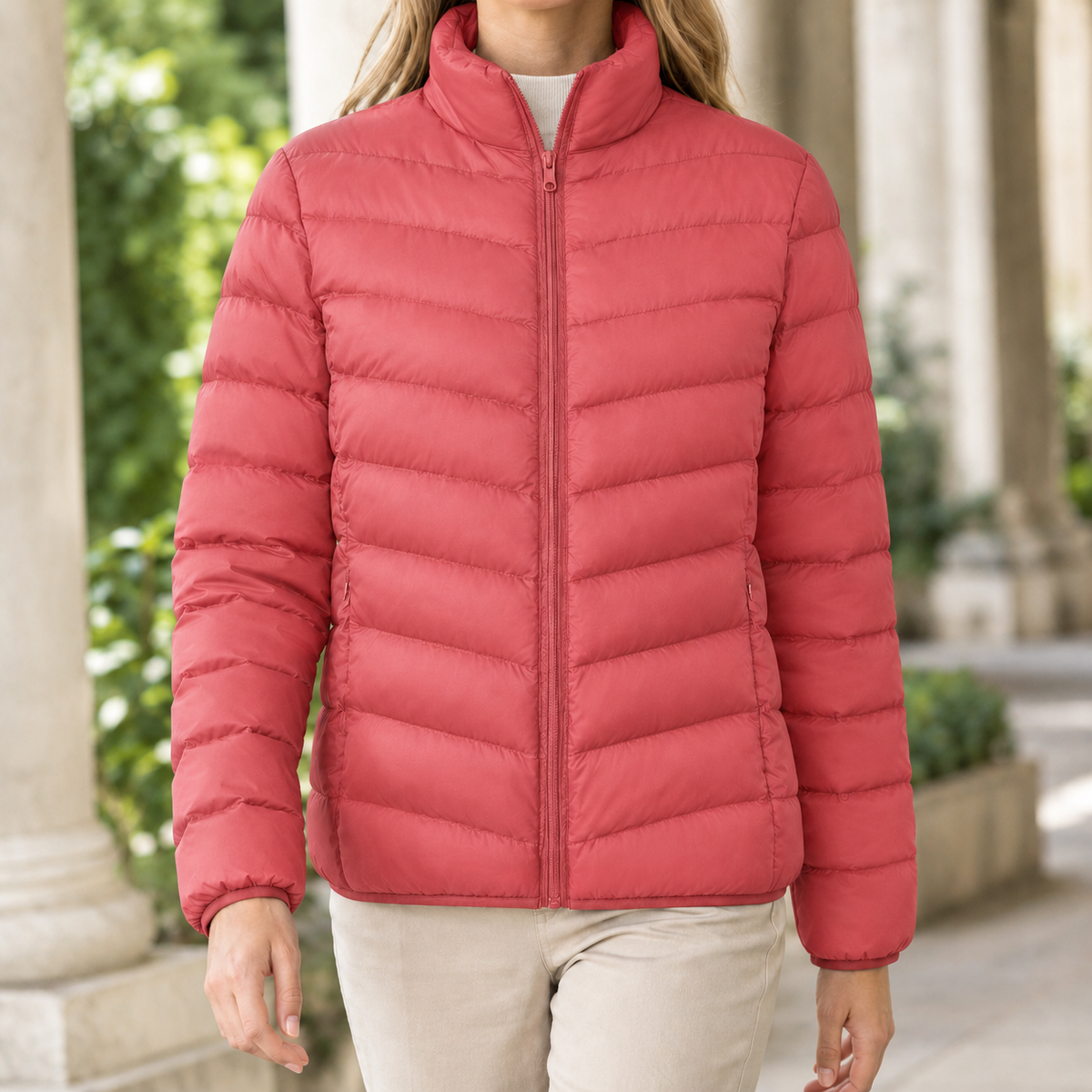 A woman wears a bright red quilted puffer jacket with chevron quilting, a stand collar and front zip.