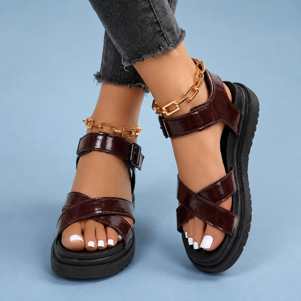 Maroon sandals with crossover straps, worn with crossed ankles.