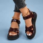 Maroon sandals with crossover straps, worn with crossed ankles.